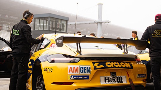 Gelber SR Porsche 718 Cayman GT4 mit Sponsoren-Decals in der Boxengasse am Nürburgring
